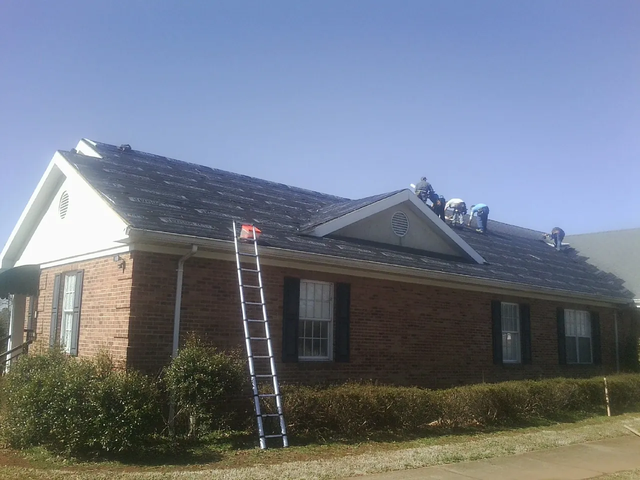 Crew tearing shingles off a brick ranch roof with a ladder set — Emergency Roof Repair work by our crew in Sardinia