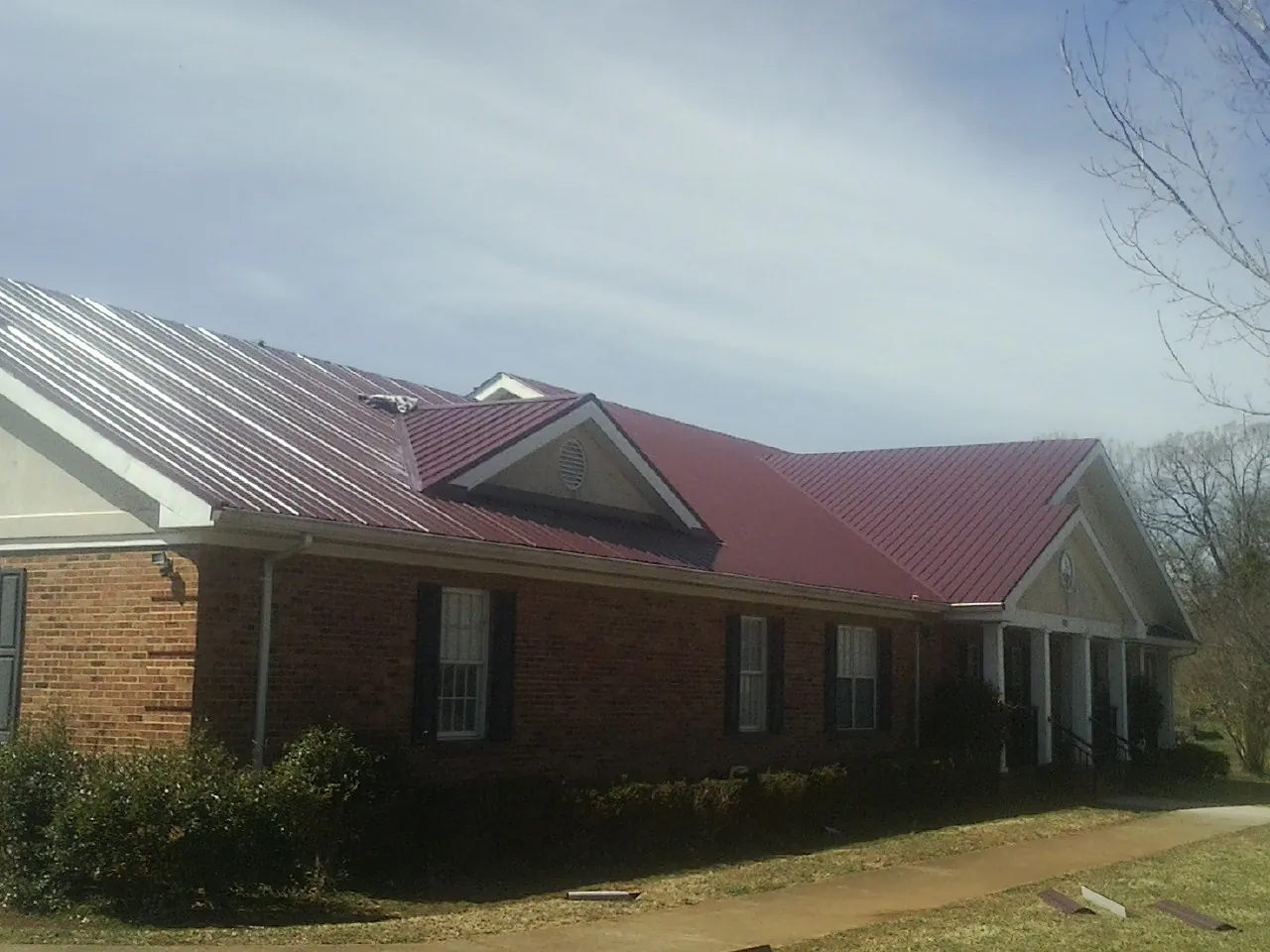 Red metal roof with gabled entries on a long brick building, from a Hail Damage Roof Repair job in Sardinia