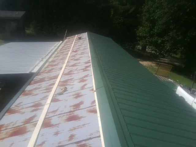 Old rusted panels beside newly installed green metal roofing — Wind Damage Roof Repair by Roofing Brothers in Sardinia