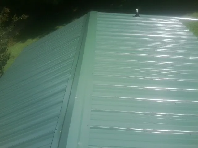 New green metal panels meeting at the ridge of a roof — Flat Roof Repair work by our crew in Sardinia